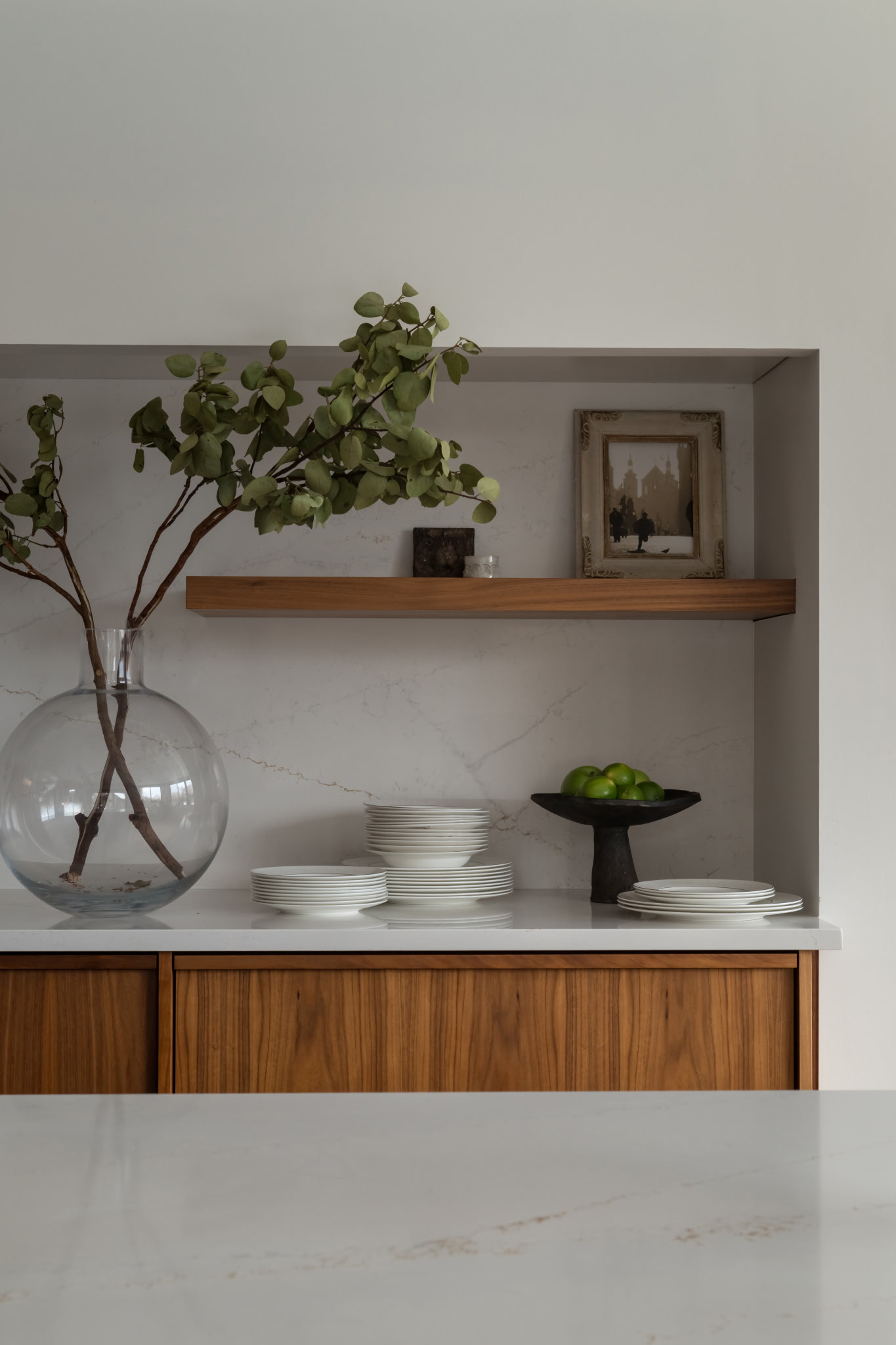 Walnut open shelving styled with stacked white dinnerware and a vintage framed print