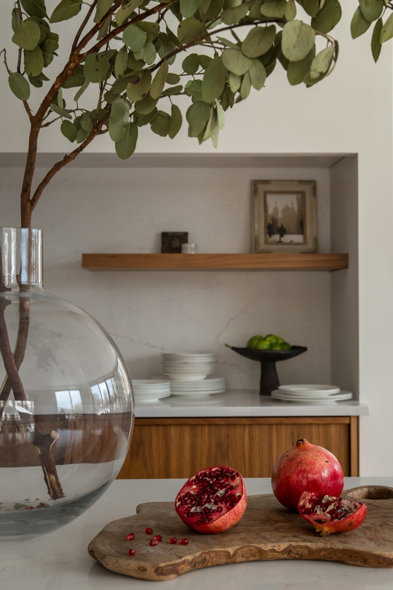 Pomegranates cut open on a wooden board beside a glass vase